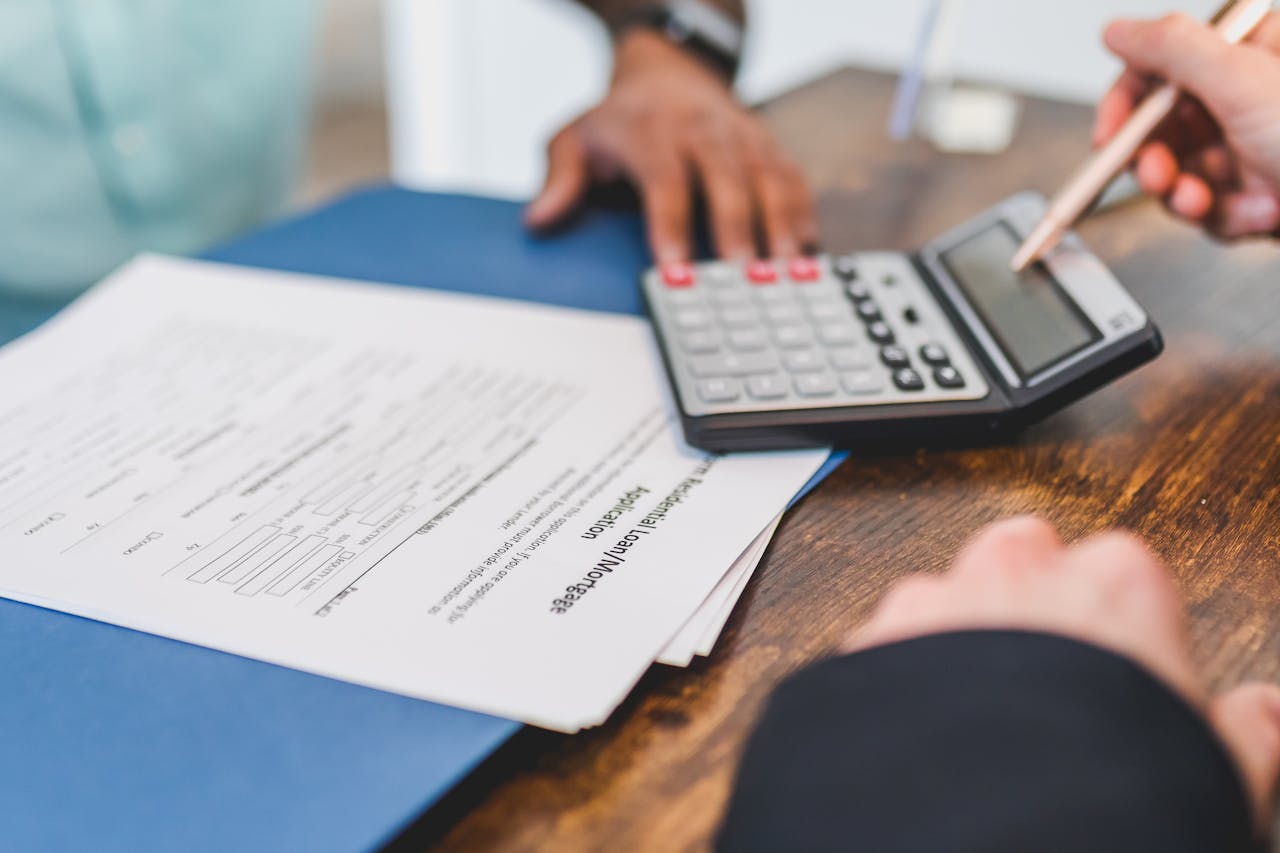 digital Hands using a calculator with real estate documents on a desk, indicating a financial transaction or meeting.